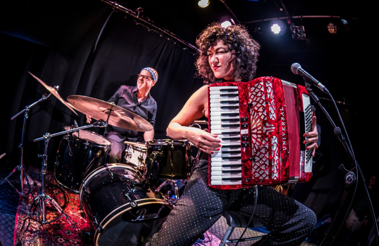 mujer en escenario con acordeón, detrás una batería