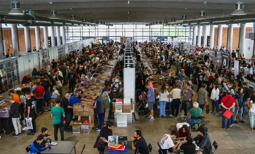 pabellón lleno de mesas con material musical, aglomeración de gente alrededor, zona de mesas y sillas