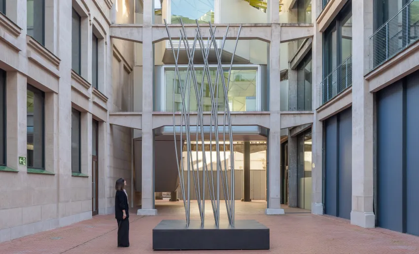en medio del patio de Serreria Belga hay una escultura de gran altura compuesta por barras metálicas torcidas, una mujer la observa