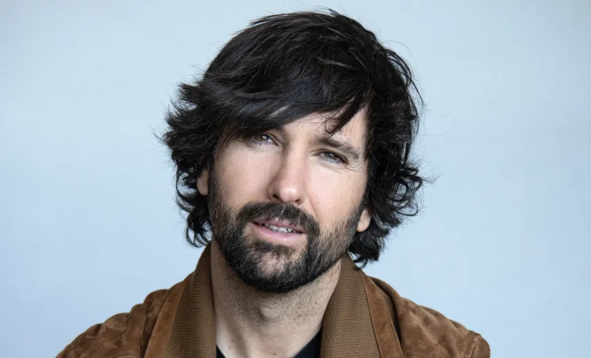 foto de frente de hombre con pelo moreno y barba, chaqueta  marrón, leve sonrisa