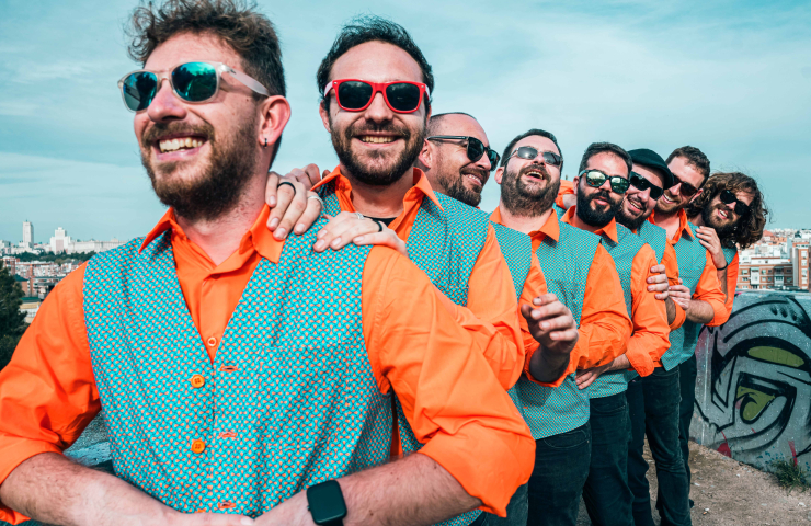 componentes del grupo en fila, todos con gafas de sol, camisa naranja y chaleco verde